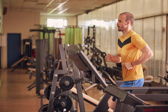 One Young Man, Wearing Sport Clothes, Traning On Treadmill, Old Beaten Up Gym Indoors. Profile View.