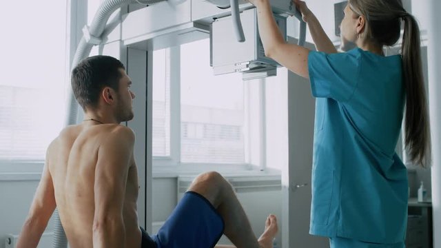 In the Hospital, Man Sitting on a Bed, Female Technician adjusts X-Ray Machine for Scanning His Leg for Injury. Scanning for Fractures, Broken Limbs, Cancer or Tumor. 