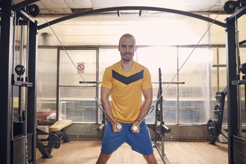 one young man smirking, wearing sport clothes, exercise on resistance bands, in old beaten up gym interior.western shot.