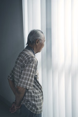 Lonely senior man standing by the window