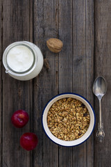 Bowl with Granola or Muesli and a jar of milk or plain yogurt with a spoon on a vintage wood background. Healthy breakfast top view composition