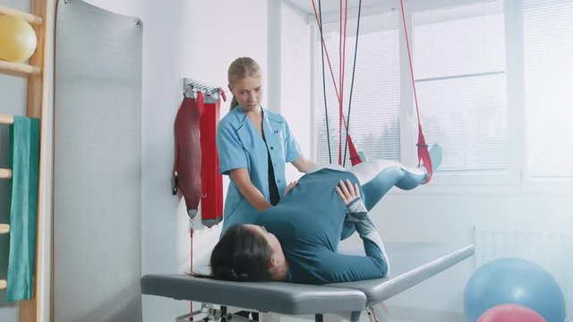 Physiotherapist Assists Female Patient with Injury, Undergoing Rehabilitative Physiotherapy on a Special Suspension Rope System. Relieving Back Pain. Shot on RED EPIC-W 8K Helium Cinema Camera.