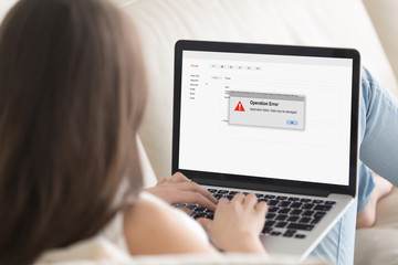 Woman lying on sofa looking at laptop screen, Operation Error message pop up. Computer crashed, software failure during web browsing, watching movie, video call or chatting via social media. Close up.