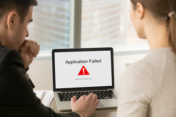 Two business people looking at laptop screen with Application Failed error message. Businessman...