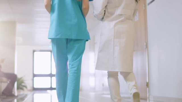 Low Angle Shot of the Nurse and Doctor Walk Through Hospital Hallway, Talking, Discussing Modern Medical Procedures. Professional People Saving Lives. Shot on RED EPIC-W 8K Helium Cinema Camera.