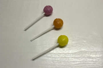 Three purple,yellow and Orange Lollipops isolated on a White textured background