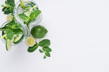 Cooking fresh summer organic drink with slices cucumber, ice, lime, mint, straw on white wood background, top view, border. Healthy detox fresh water.