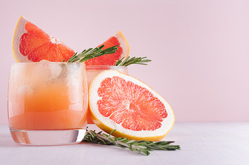 Cold grapefruit cocktail with ice, rosemary and pieces grapefruit on pastel pink background, closeup. Fresh summer healthy diet beverage. © finepoints