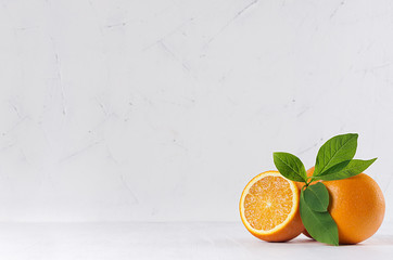 Citrus with half juicy oranges and green leaves on white wood table.