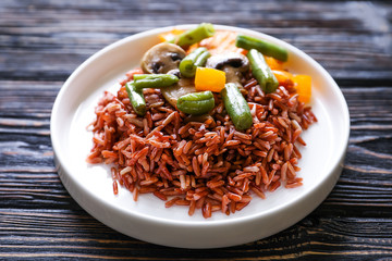 Plate with delicious brown rice and vegetables on wooden background