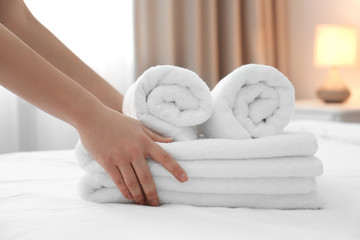Chambermaid with stack of towels on bed in hotel room