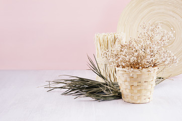 Gentle spring vanilla background with white dry flowers and green branches and bamboo dish on light table and pink wall.
