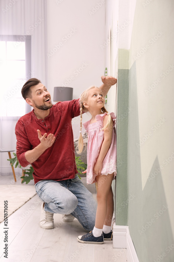 Poster Young man measuring his daughter's height at home