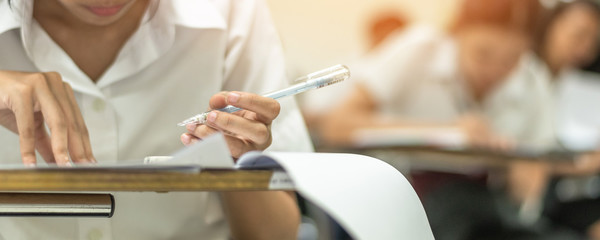 School student's taking exam, thinking hard, writing answer with left hand in classroom for educational university admission test  and world literacy day concept