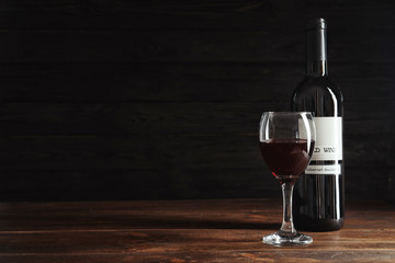 Glass and bottle with delicious red wine on table against dark background