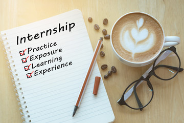 Concept Internship benefits message on notebook with glasses, pencil and coffee cup on wooden table.