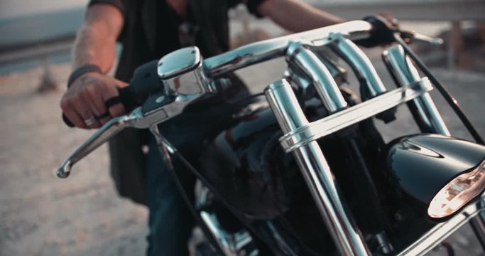 Close-up of macho man's hands with tattoos on motorcycle handlebar