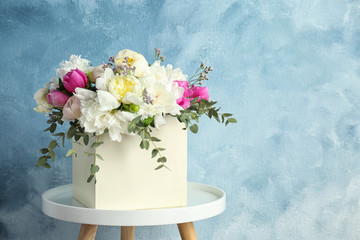 Box with bouquet of beautiful flowers on table against color background