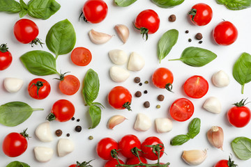 Flat lay composition with tomatoes, mozzarella cheese balls, garlic and basil on light background