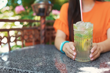 Young woman with glass of tasty lemonade at table in cafe, outdoors. Natural detox drink