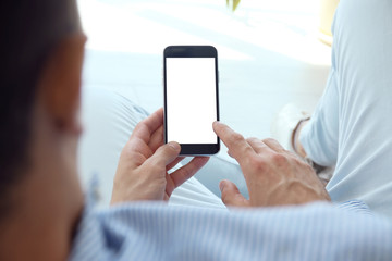 Young man holding mobile phone with blank screen in hand, indoors