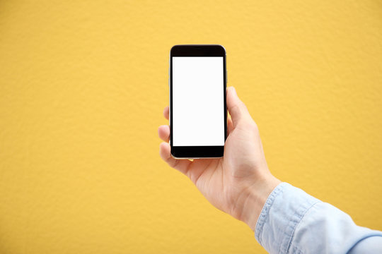 Young Man Holding Mobile Phone With Blank Screen In Hand On Color Background