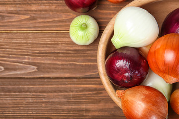 Bowl with fresh ripe onions on wooden background, top view