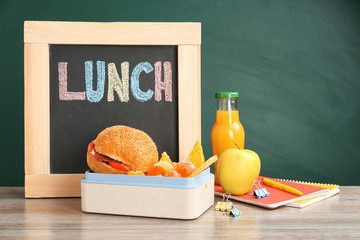 Lunch box with appetizing food, small blackboard and notebooks on table