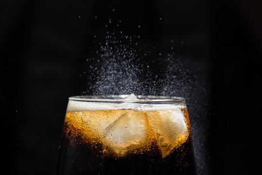 A glass of cola beverage with a salt close-up. On a black background.