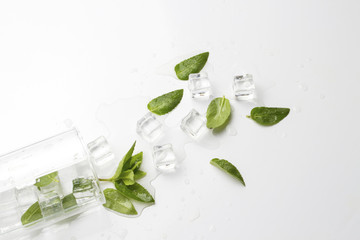 Spilled Glass with refreshing water, mint leaves and ice cubes on a light background