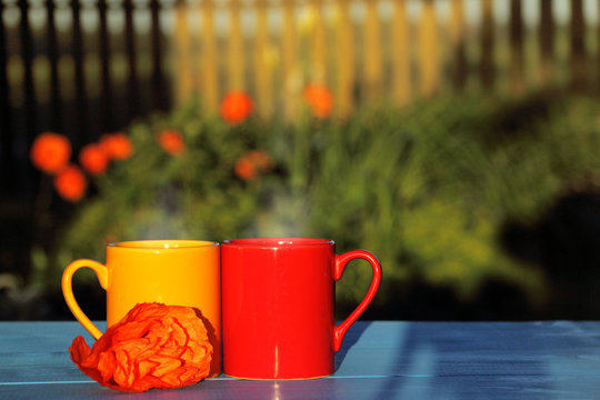 romantic atmosphere with hot drinks/ two mugs decorated with a poppy flower against a background of flower beds in the garden 