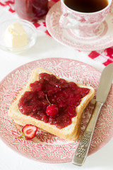 Breakfast of bread toasts with butter and strawberry-rhubarb jam, served with tea. Rustic style.