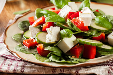 Fresh spinach salad with feta, cucumber and red paprika on a plate.