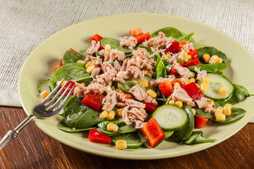 Fresh spinach salad with tuna, cucumber, corn, and red paprika on a plate