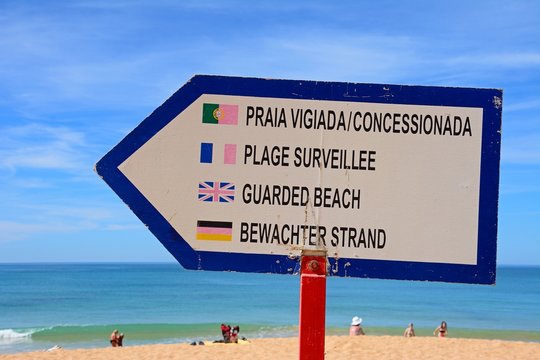 Multilingual guarded beach sign on the beach with the ocean to the rear, Albufeira, Algarve, Portugal.
