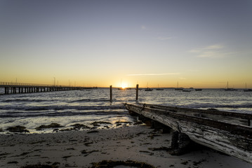 The sun rising over the horizon by the end of the Flinders pier on the Mornington peninsula, Victoria, Australia with the sun positioned between two pillars of an old boat launch ramp