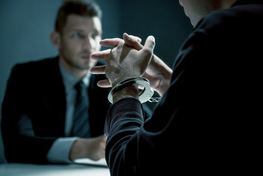 Criminal man with handcuffs being interviewed in interrogation room