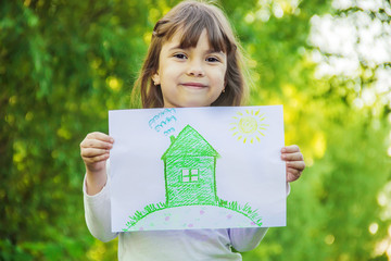 Drawing of a green house in the hands of a child. Selective focus. 