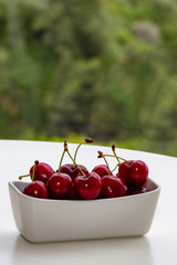 large cherry in a white vase on a white table. Background of a green garden. Vertically.