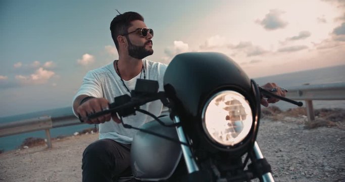Young macho man with tattoos on motorcycle looking at sunset
