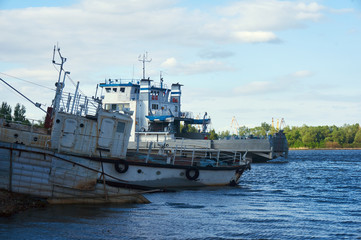 Obraz premium The old boat and the ferry at the shore on the river on a sunny summer day.