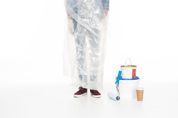 cropped image of man in polyethylene cover standing near paint tins, paint roller and coffee cup isolated on white background