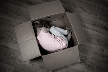 A sad little child lies in a box on the floor. The concept of isolation, loneliness, running away...