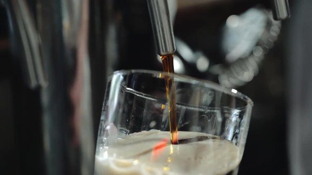 Bartender pours a dark beer in glass. Close-up.