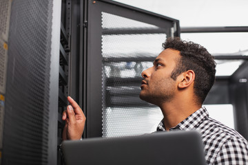 IT technician. Low angle of handsome IT guy using laptop and scrutinizing hardware
