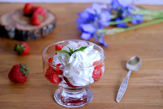 Summer dessert, sliced strawberry with whipped cream in a glass vase. Summer concept