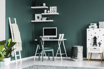 Study space for a teenager in a dark green bedroom interior with white shelves with decorations and...