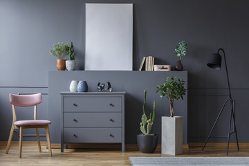 Grey cabinet between wooden chair and plants in living room interior with mockup of poster. Real...