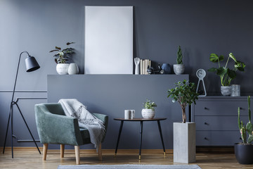 Green armchair next to black table and plant in living room interior with mockup of poster. Real...