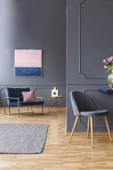 Real photo of a grey, spacious living room with a wooden floor and grey rug next to a chair and in front of the other, wider blue chair
